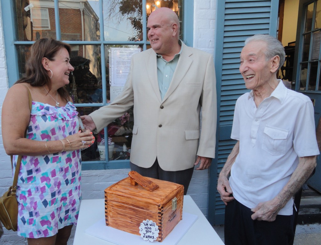 Master cobbler James Spinelli (right) is presented with a custom cake in honor of his retirement. Haddonfield Commissioner Neal Rochford (center) and Retail Recruiter Remi Fortunato celebrated his years of operation in the borough. Credit: Matt Skoufalos.